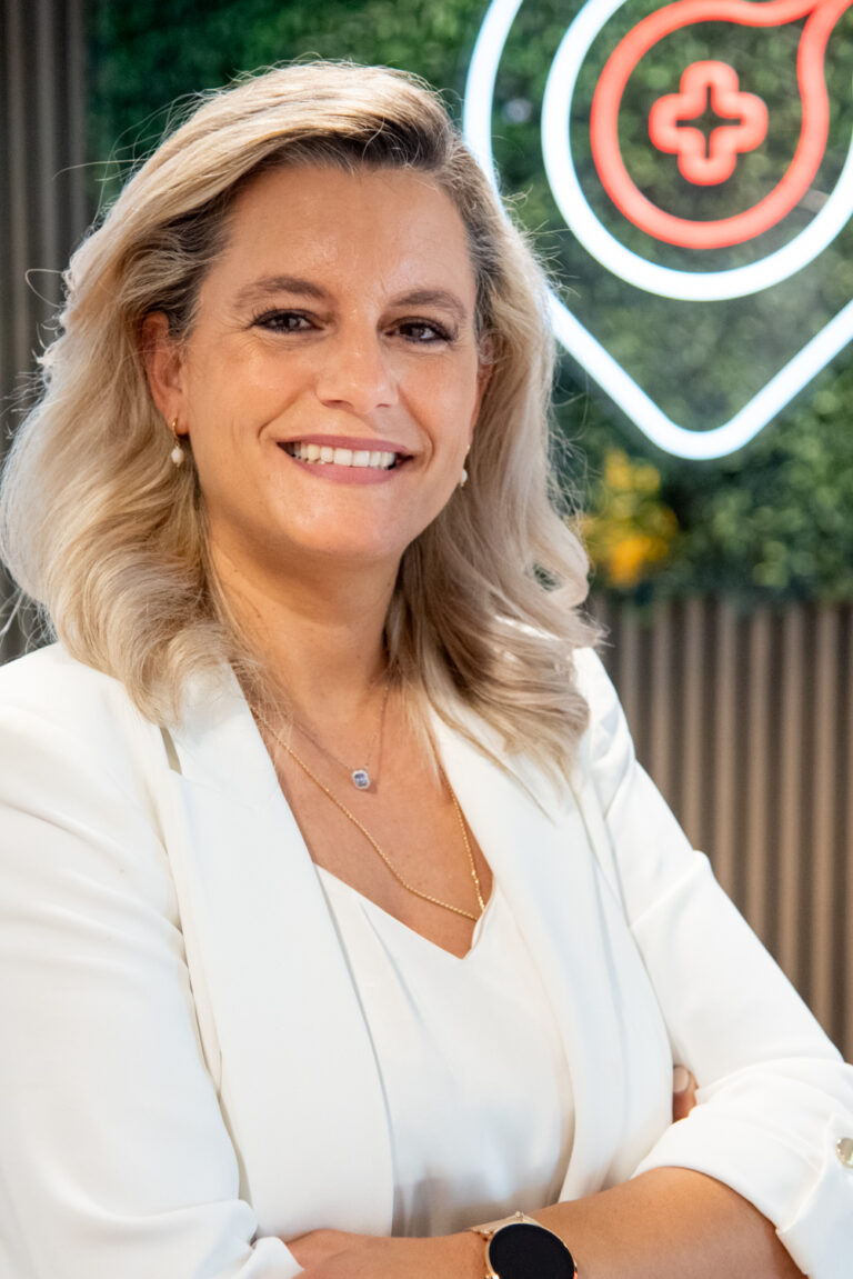 Smiling woman in white blazer in front of logo